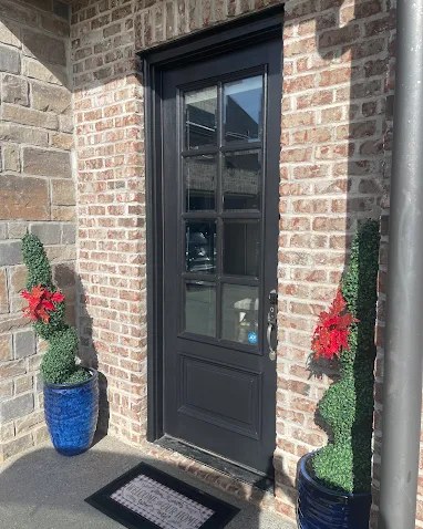 A freshly painted black front door with glass panels set in brick, flanked by boxwoods