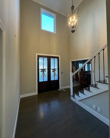 Repainted two-story entry foyer with white trim, glass front doors, and dark hardwood floors